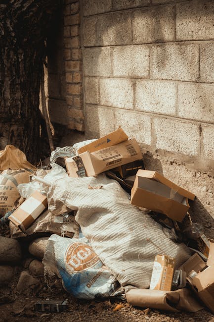 A collection of discarded household items and debris scattered on a paved outdoor surface, including a broken wooden garden bench with slatted legs leaning against a wall, a damaged white cabinet with